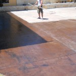 A man is holding a hose while standing on the cement.