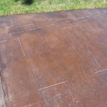 A concrete patio with brown stain and grass.