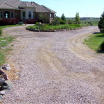 A gravel driveway leading to a house with a large yard.