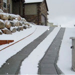 A snowy driveway with steps leading to the house.