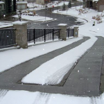 A sidewalk with snow on the ground and a fence.