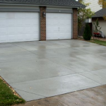 A driveway with two white doors and grass growing on the side.