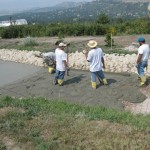 Three men in white shirts and yellow boots are working on a road.