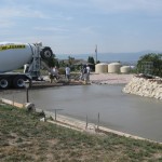 A cement truck is pouring concrete on the side of a road.