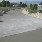 A concrete driveway with a bench and rock wall.