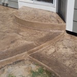 A concrete patio with steps leading to the front door.