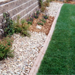 A garden with grass and rocks next to the side of a wall.