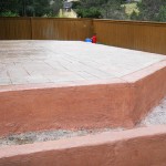 A cement patio with a red umbrella on the side.